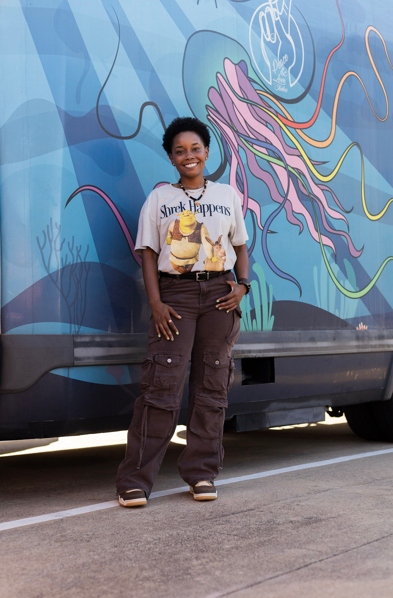 Jelly Robinson standing in front of her mobile Peace & Love Studios truck, painted with a jellyfish and peace-sign hand mural